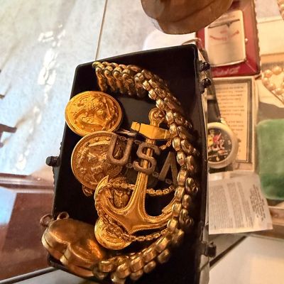 Small tray of vintage costume jewelry and military pins, including a gold-tone anchor motif pendant, a USA insignia pin, and a chain link...