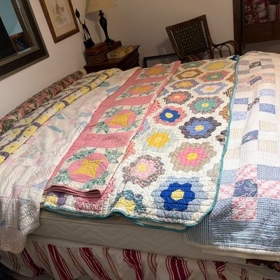 Sale Photo Thumbnail #192: Collection of vintage handmade quilts in various colorful patterns, including Grandmother's Flower Garden and patchwork designs, displayed across a bed.