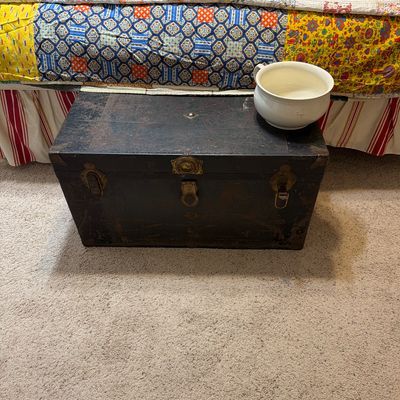 Sale Photo Thumbnail #191: Antique dark-stained wooden trunk with metal hardware and latches, shown with a white ceramic chamber pot resting on top.