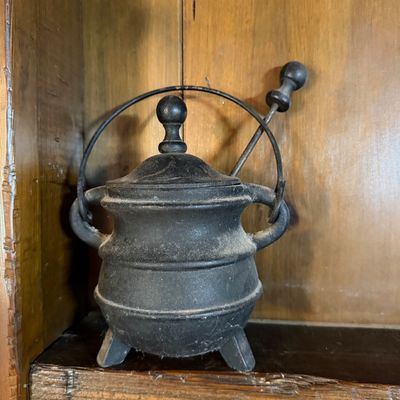 Vintage miniature cast iron cauldron with lid, wire handle, and matching pestle, showing a dusty, aged patina.