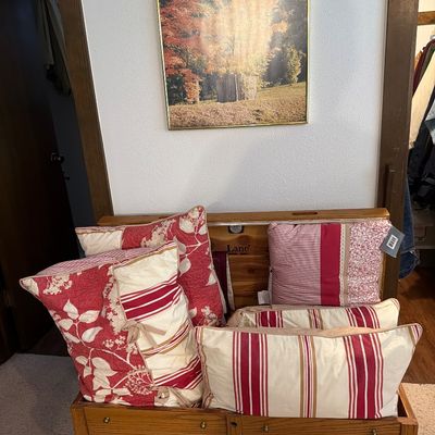 Sale Photo Thumbnail #200: Vintage Lane cedar chest with faux drawer fronts, filled with assorted red and cream patterned throw pillows, positioned beneath a framed autumn landscape print.
