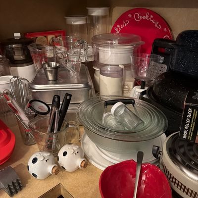 Sale Photo Thumbnail #146: Assorted kitchenware including Pyrex glass mixing bowls, measuring cups, a red ceramic bowl with ladle, novelty pig salt and pepper shakers, and various baking pans.