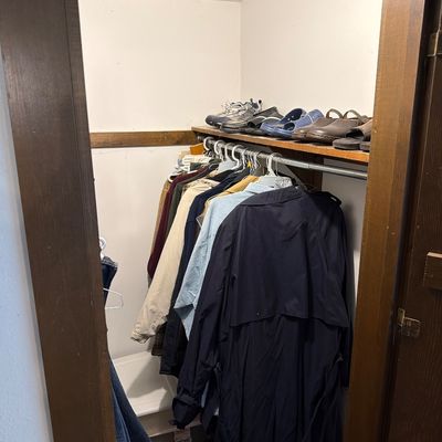 Sale Photo Thumbnail #201: Assorted men's outerwear, including a navy trench coat and light jackets, hanging in a closet beneath a shelf of casual shoes and sandals.