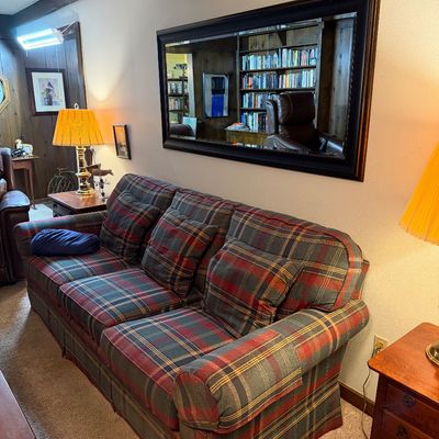 Sale Photo Thumbnail #105: Three-cushion sofa upholstered in a classic red, green, and yellow plaid fabric, paired with matching throw pillows and positioned beneath a large dark-framed wall mirror.