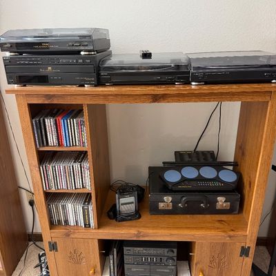Wooden media console cabinet featuring built-in CD storage shelves, lower cabinets with carved wheat details, and various vintage audio...