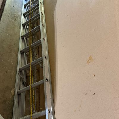 Sale Photo Thumbnail #272: Heavy-duty aluminum extension ladder with pulley system and yellow rope, leaning against a wall.