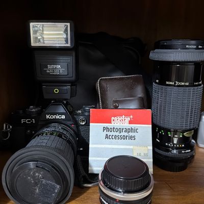 Sale Photo Thumbnail #163: Konica FC-1 35mm SLR camera with a Sunpak auto 322 D flash, a Sigma Zoom-K II 70-210mm lens, and various vintage photographic accessories.