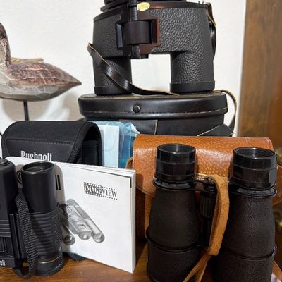 Sale Photo Thumbnail #164: Collection of vintage and modern binoculars, including a large black pair with a leather case, a smaller black pair with a tan leather case, and a Bushnell ImageView digital camera binocular set with its manual.