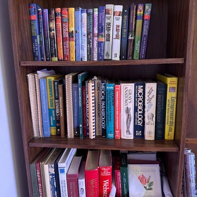 Sale Photo Thumbnail #152: Three-shelf wooden bookcase filled with books, including a collection of Charlaine Harris novels, medical textbooks like Gray's Anatomy, and reference dictionaries.