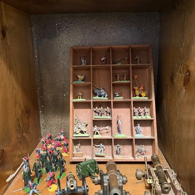 Collection of vintage miniature toy soldiers and model cannons, featuring hand-painted metal figurines displayed in a wooden shadow box...