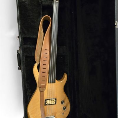 Carvin fretless electric bass guitar with natural wood finish, tan leather strap, and hard-shell velvet-lined case.