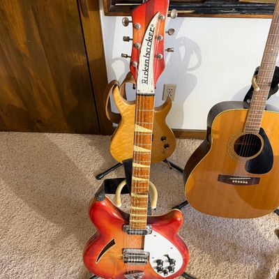 Vintage Rickenbacker semi-hollowbody electric guitar in Fireglo finish, displayed on a stand alongside other guitars.