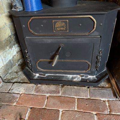 Vintage Heat King black cast iron wood-burning stove insert with brass trim and a coiled wire handle, shown sitting on a brick hearth.