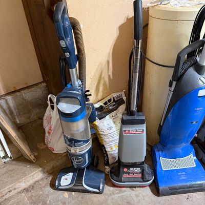 Sale Photo Thumbnail #276: Collection of floor cleaning equipment, including a Hoover React upright vacuum, a Hoover FloorMax hard floor cleaner, and a bright blue Miele upright vacuum.