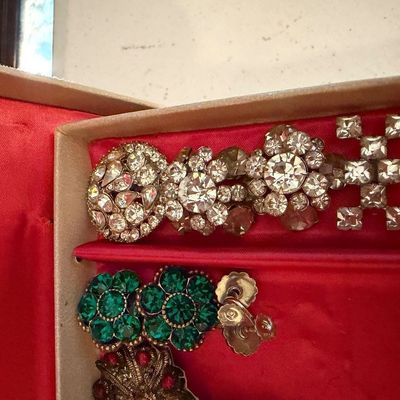 Sale Photo Thumbnail #116: Collection of vintage rhinestone costume jewelry, including green flower-shaped clip-on earrings and clear rhinestone brooches, presented in a red-lined box.