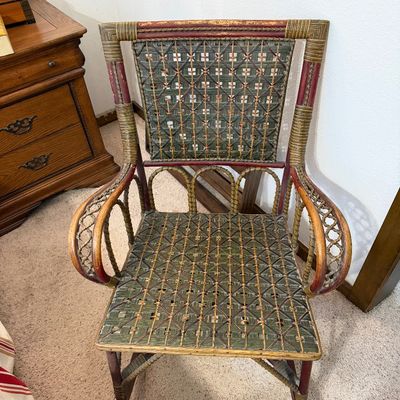 Vintage wicker and rattan rocking chair with green and red painted accents, featuring an intricate woven seat and backrest.