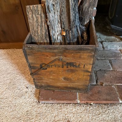 Sale Photo Thumbnail #157: Vintage wooden crate with a wire handle, filled with firewood and showing a faded stencil logo on the front.