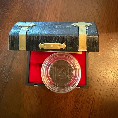 Sale Photo Thumbnail #253: Collectible coin housed in a protective plastic capsule, presented inside a small, black treasure chest-style box with a red velvet-lined interior.