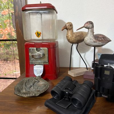 Vintage red Oak 1-cent gumball machine alongside two carved wooden shorebird decoys, a pair of black binoculars, and a brass anchor-motif...