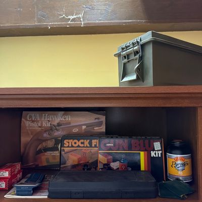 Sale Photo Thumbnail #170: Assorted shooting and gun maintenance supplies, including a CVA Hawken Pistol Kit box, Hoppe's Gun Blue Kit, Pyrodex propellant, and a green plastic ammo can.
