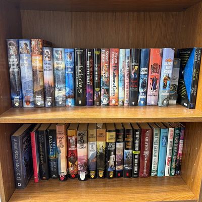 Sale Photo Thumbnail #179: A collection of fantasy and science fiction paperback books, including titles by Terry Goodkind, Sara Douglass, and Steven Erikson, arranged on wooden bookshelves.