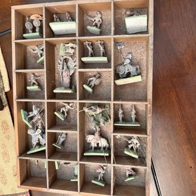 Vintage miniature lead or metal military figurines, including cavalry and infantry, stored in a divided wooden shadow box with visible...