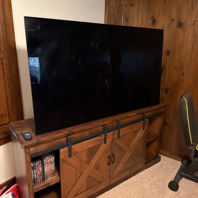 Large flat-screen television sitting on a rustic wooden media console with sliding barn-style doors and open shelving.