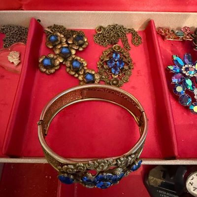 Assortment of vintage costume jewelry featuring blue rhinestones, including a hinged bangle bracelet, a cross pendant, and an oval...