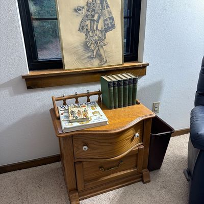 Sale Photo Thumbnail #187: Vintage oak nightstand with a serpentine drawer front, spindle gallery rail, and two drawers, styled with books and a framed sketch of a historical figure.