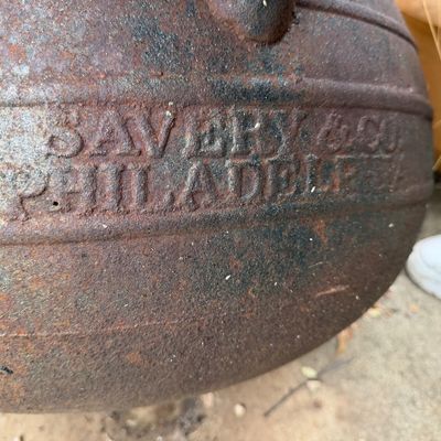 Close-up of a rustic, antique Savery & Co. Philadelphia cast iron cauldron showing significant surface rust and embossed lettering.