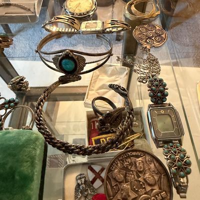 Collection of vintage jewelry and watches displayed inside a glass case, including Native American turquoise cuff bracelets, vintage...