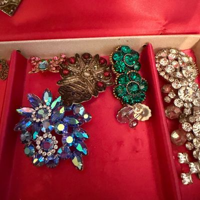 Assortment of vintage costume jewelry, including rhinestone brooches and clip-on earrings in vibrant blue, green, and clear stones,...
