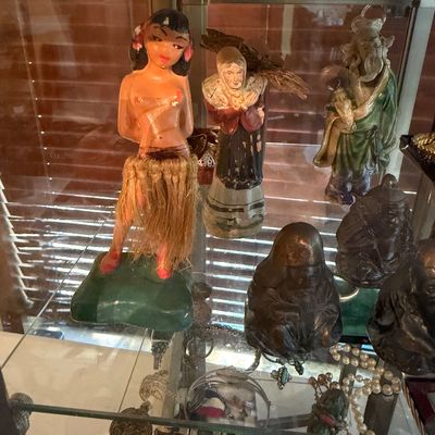 Collection of vintage decorative figurines displayed inside a glass cabinet, featuring a mid-century hula girl nodder with raffia skirt...
