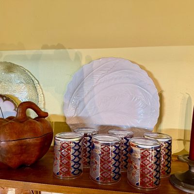Sale Photo Thumbnail #130: Collection of tabletop decor including a set of six patterned tumblers, a carved wooden pumpkin container, decorative ceramic platters, and a pair of pewter candle holders with red taper candles.