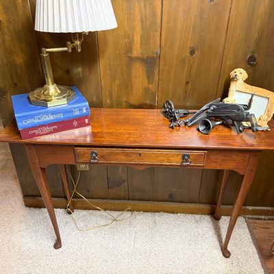 Queen Anne style cherry console table with a single drawer, cabriole legs, and pad feet, shown with a brass swing-arm lamp and decorative...