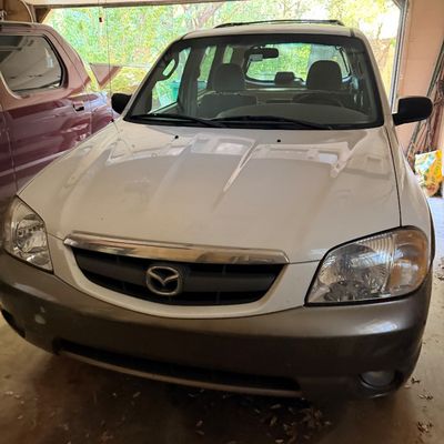 White Mazda Tribute SUV with a grey lower bumper, parked inside a garage.