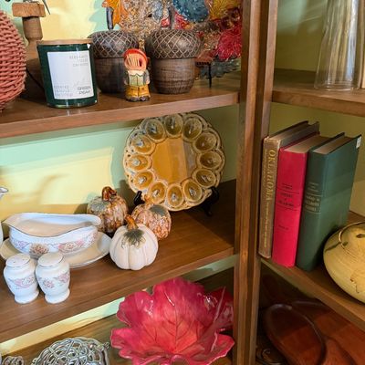 Sale Photo Thumbnail #123: Wooden shelving unit filled with fall-themed home decor, including glazed ceramic pumpkins, leaf-shaped bowls, acorn canisters, and a yellow glazed deviled egg platter.