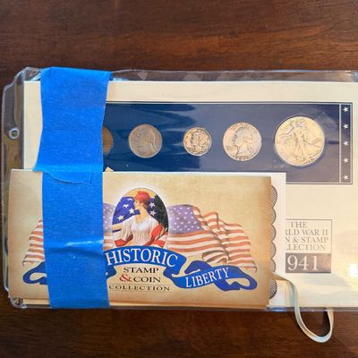 Sale Photo Thumbnail #214: The World War II Coin & Stamp Collection from 1941, featuring a set of five US coins and a Historic Stamp & Coin Liberty booklet secured with blue tape.