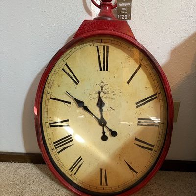 Sale Photo Thumbnail #110: Large oval wall clock from Pier 1 Imports, featuring a distressed red frame designed to look like a pocket watch, Roman numerals, and a vintage-style face reading 'Cafe des Marguerites'.