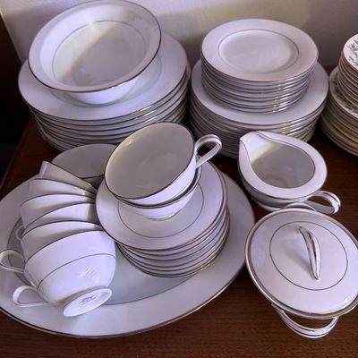 Sale Photo Thumbnail #151: Vintage white porcelain dinnerware set with silver trim, including plates, bowls, teacups, saucers, a creamer, and a lidded sugar bowl.