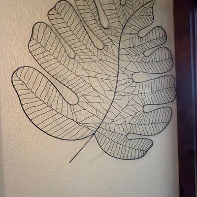 Sale Photo Thumbnail #189: Large wirework wall sculpture depicting a monstera leaf, featuring a detailed vein pattern and a rustic dark metal finish.