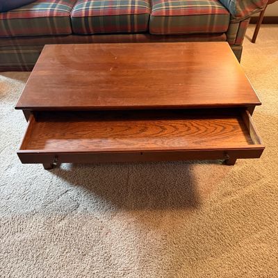 Traditional oak coffee table featuring a large pull-out storage drawer, shown in front of a plaid sofa.