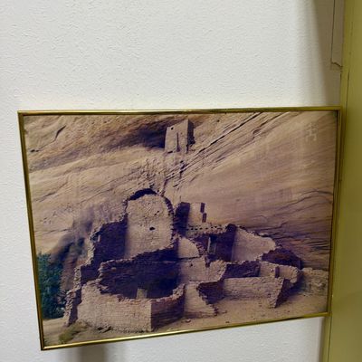 Sale Photo Thumbnail #172: Framed photograph depicting ancient cliff dwellings, likely Mesa Verde or a similar Southwestern archaeological site, housed in a simple gold-toned metal frame.