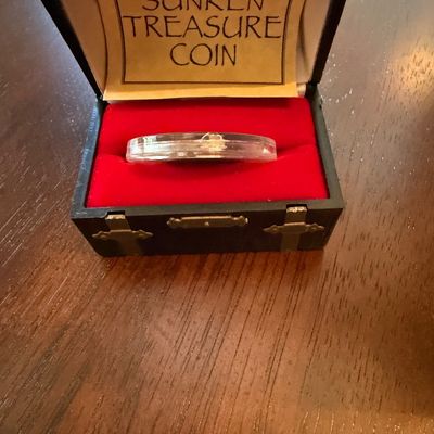 Sale Photo Thumbnail #254: Collectible "Sunken Treasure Coin" housed in a protective plastic capsule, presented inside a small black treasure chest-style display box with a red velvet interior.
