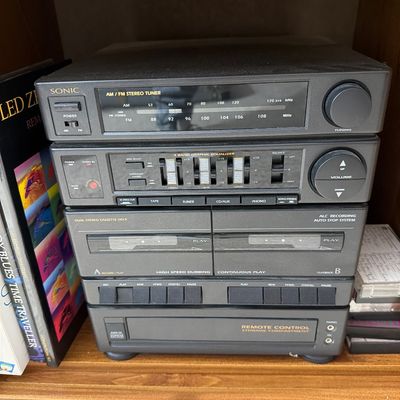 Sale Photo Thumbnail #181: Vintage Sonic brand compact stereo system featuring an AM/FM tuner, 3-band graphic equalizer, and dual cassette deck, housed in a black plastic casing.