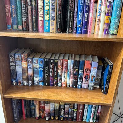 Three shelves of fantasy and science fiction paperback books, including titles by Stephen R. Donaldson, Sara Douglass, and Arthur C....