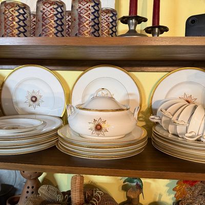 Collection of vintage white porcelain dinnerware featuring gold rims, starburst motifs, a covered tureen, stacked plates, and teacups.