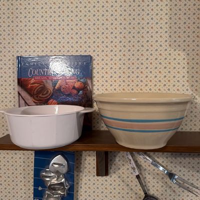 Sale Photo Thumbnail #141: Vintage kitchenware collection featuring a yellowware mixing bowl with blue and pink stripes, a white CorningWare casserole dish, a Country Baking cookbook, and metal cookie cutters.