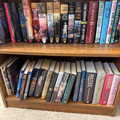 A collection of fantasy and sci-fi paperback and hardcover books, including titles by Terry Goodkind, Neil Gaiman, and David Eddings,...