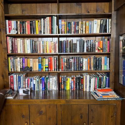 Sale Photo Thumbnail #138: Large rustic pine built-in bookcase cabinet filled with a diverse collection of vintage hardcover and paperback books.